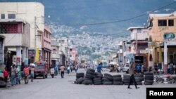 La gente camina en una calle tranquila parcialmente bloqueada con una barricada hecha con neumáticos, generalmente llena de gente y tráfico pesado en Puerto Príncipe, Haití, 13 de octubre de 2022.