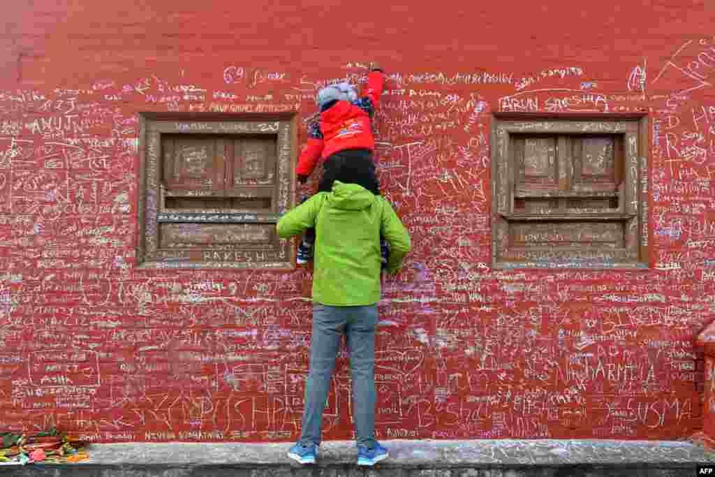 A child, helped by his father, writes a message with chalk on a wall at the Saraswati temple on the occasion of the Hindu festival of &#39;Basanta Panchami&#39;, in Kathmandu, Nepal.