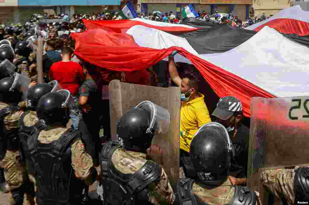 Iraqi security forces stand in front of demonstrators in anti-government protests during Iraqi Prime Minister Mustafa al-Kadhimi's visit, in Basra.
