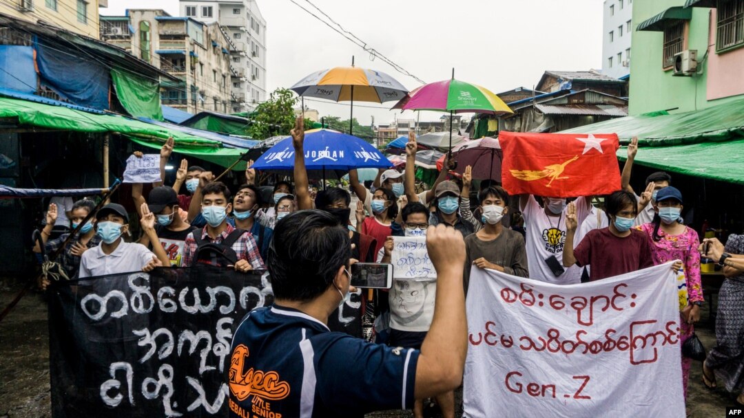 FILE - A man records protesters on his mobile phone as they take part in a demonstration against the military coup, in Yangon, Myanmar, May 21, 2021. 