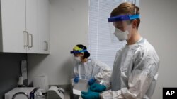 FILE - Wayne State University medical school students Lucia Luna-Wong, left and Michael Moentmann work in a COVID-19 testing center in Detroit, April 24, 2020.