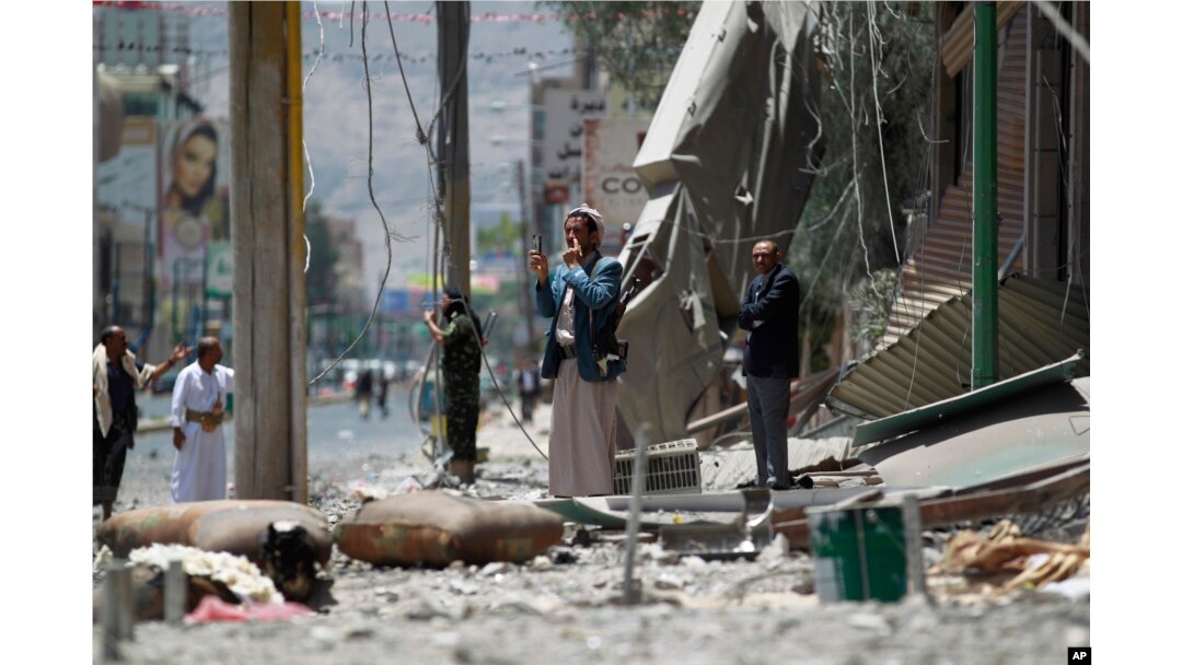 FILE - A man uses his cell phone to take pictures of houses destroyed by a Saudi-led airstrike in Sana'a, Yemen, June 8, 2015.
