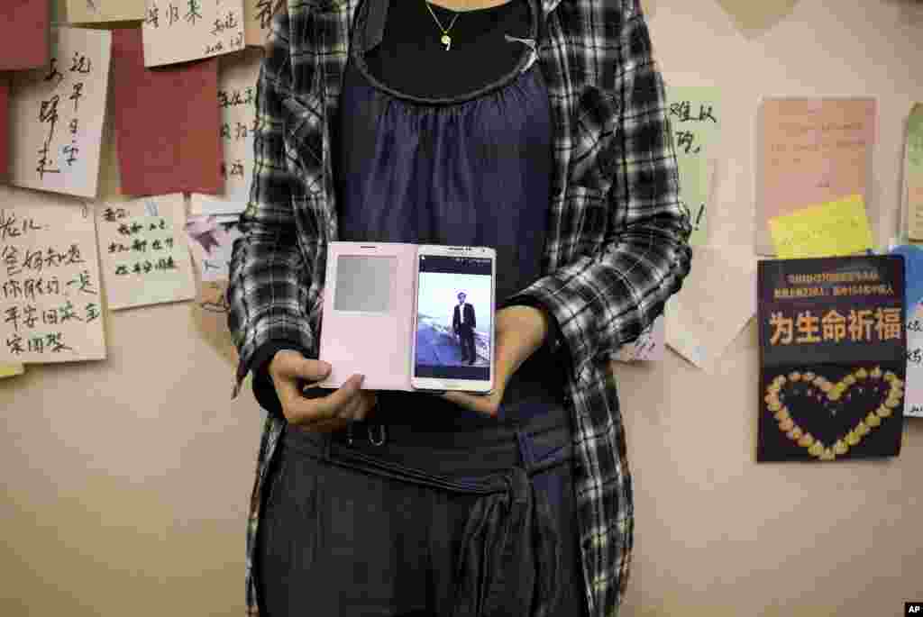 Anak perempuan seorang penumpang asal China menunjukkan foto ayahnya dalam ponselnya, dekat dinding yang menampilkan pesan-pesan penuh harapan bagi para penumpang pesawat yang hilang di sebuah hotel di Beijing (11/4). (AP/Andy Wong)