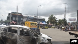 A police officer gestures next to a burnt out car that was set on fire during protests against a third term for Ivorian President Alassane Ouattara, in Abidjan, Oct. 19, 2020, ahead of presidential elections set for Oct. 31, 2020.