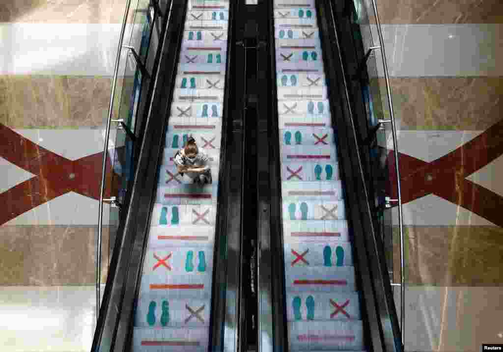 A woman wearing a protective face mask stands in an escalator with marks for social distancing during reopening at Pondok Indah Mall in Jakarta, Indonesia.