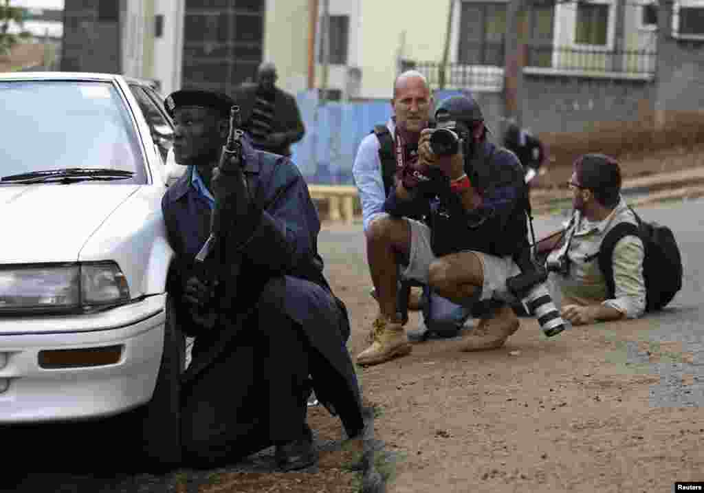 Seorang polisi dan para juru foto berlindung setelah mendengar tembakan senjata di dekat pusat perbelanjaan Westgate di Nairobi, Kenya.