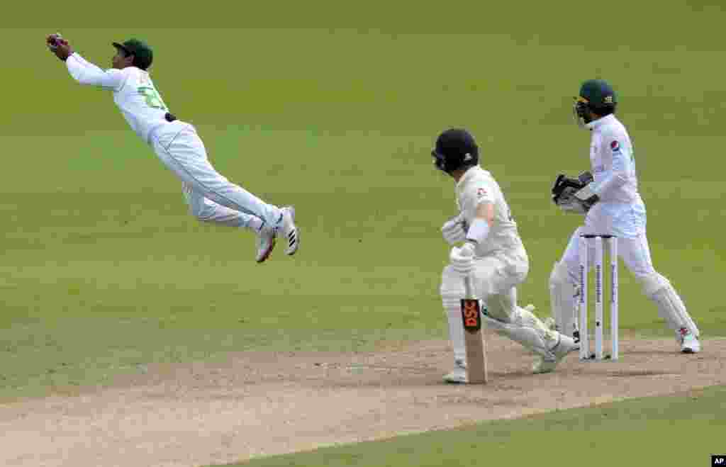 Pakistan's Asad Shafiq, left, dives to catch the ball to dismiss England's Dominic Bess, center, during the third day of the first cricket test match between England and Pakistan at Old Trafford in Manchester, England.