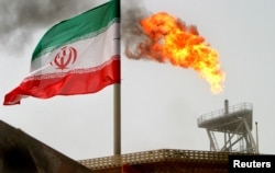 FILE - A gas flare on an oil production platform in the Soroush oil fields is seen alongside an Iranian flag in the Persian Gulf, Iran, July 25, 2005.