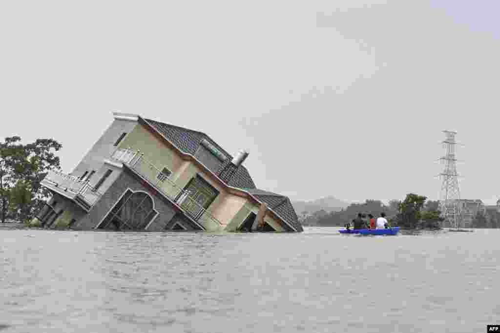 Residents ride a boat past a damaged house near the Poyang Lake due to torrential rains in Poyang county, Shangrao city in China's central Jiangxi province, July 15, 2020.