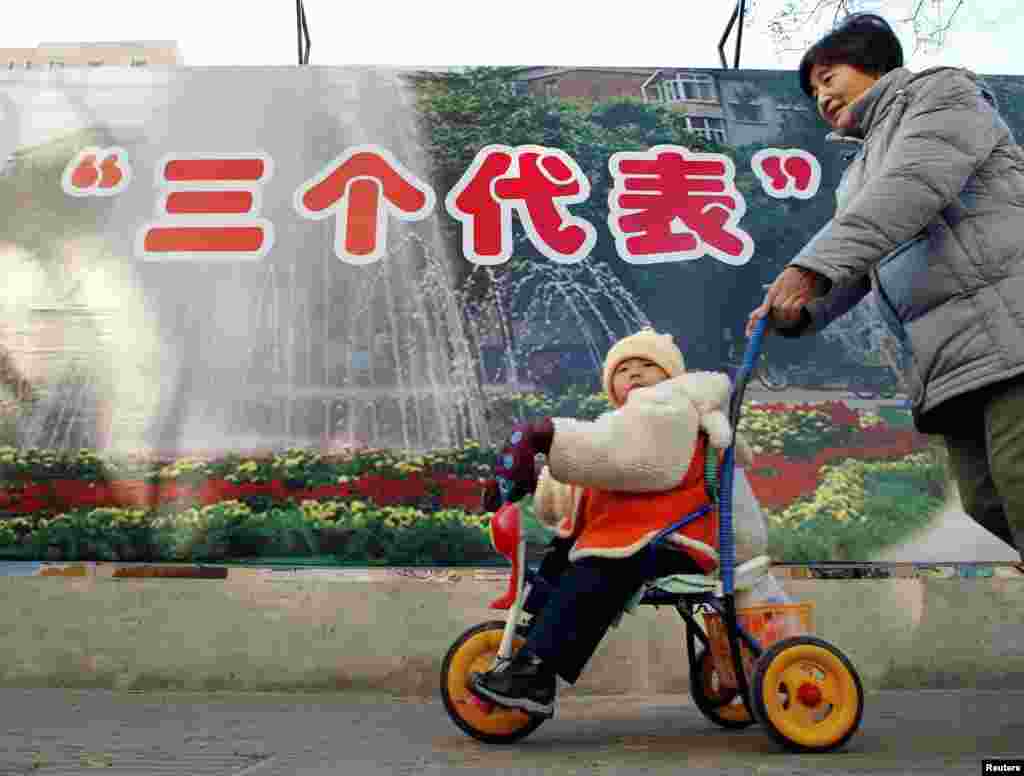 2002年11月28日,北京的一位母亲推着婴儿走过“三个代表”思想的宣传牌。“三个代表”思想被认为是江泽民的重要理论贡献。