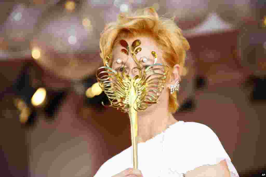 Actress Tilda Swinton holds a carnival mask as she poses for photographers upon arrival at the opening ceremony of the 77th edition of the Venice Film Festival in Venice, Italy.