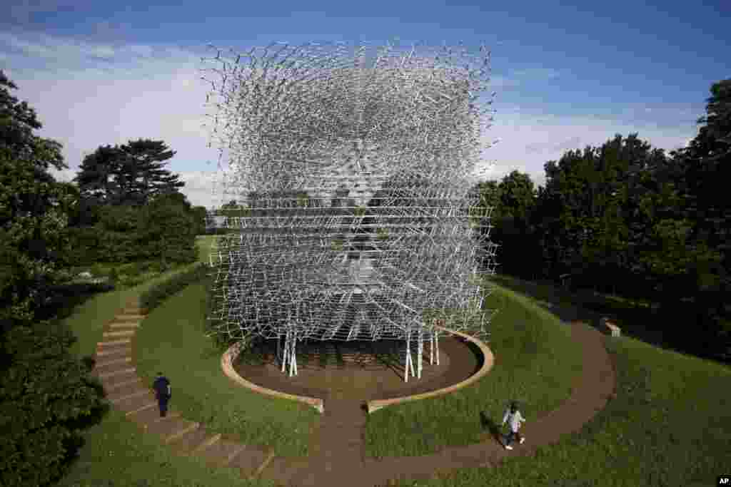 People pose for photographs by walking either side of artist Wolfgang Buttress' 17 meter high bee health inspired 'The Hive' aluminum installation as it stands on display after being put up in Kew Royal Botanic Gardens west London.