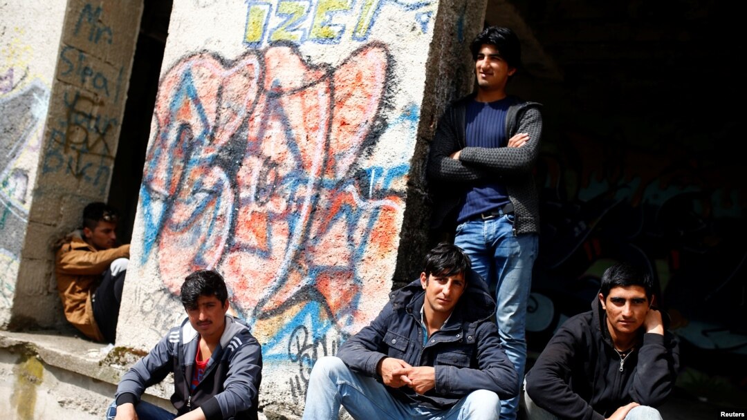 FILE - Migrants sit outside a dorm destroyed during the Bosnian 1992-1995 war, in Bihac, Bosnia and Herzegovina, May 11, 2018. 