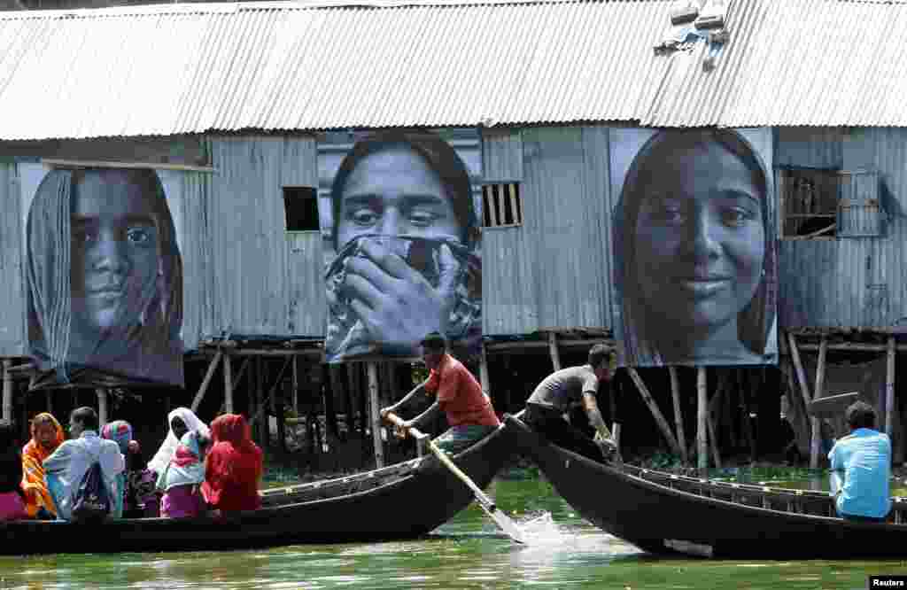 Dua perahu yang membawa orang-orang dari pemukiman kumuh melewati foto-foto pekerja garmen yang diambil oleh siswa jurusan fotografi Counter Foto, di wilayah kumuh Korail kumuh di Gulshan, Dhaka, 13 Mei 2013. Pemasangan foto dari pekerja garmen itu dilakukan untuk memperingati perempuan-perempuan Bengali yang merupakan pekerja keras dan untuk mendukung perjuangan mereka demi terciptanya keadilan sosial-ekonomi. Kegiatan itu merupakan bagian dari proyek "Martabat dalam Industri" oleh seniman Perancis J.R. dan Proyek Inside Out, seperti dikatakan oleh pihak penyelenggara.