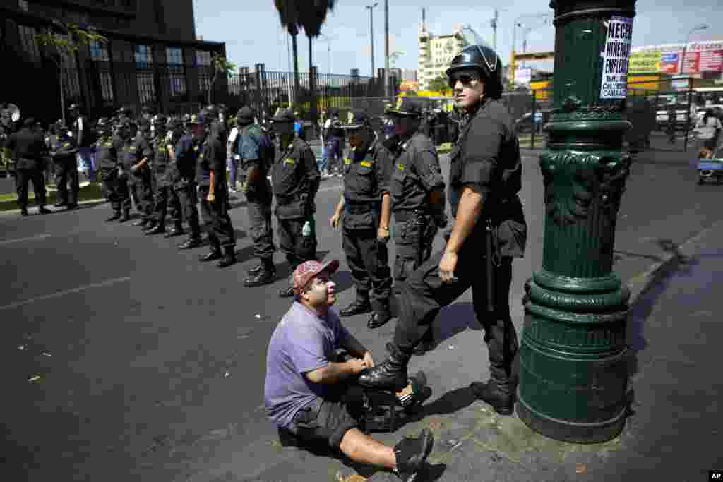 Seorang penyemir sepatu menyemir sepatu seorang polisi yang sedang mengamankan aksi demonstrasi di Lima, Peru.