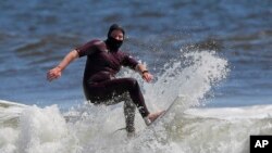 FILE - In this May 13, 2020 photo, Tim O'Rourke surfs with a face covering to protect him from the coronavirus at Venice Beach, as masks are required at Los Angeles County beaches, which reopened with restrictions.