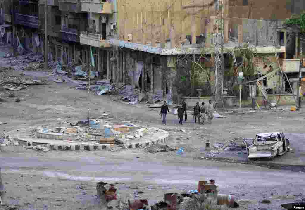 Members of the Free Syrian army walk with their weapons along a street filled with debris, Deir al-Zor, Syria, April 15, 2013.