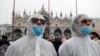 FILE - Tourists wear protective face masks at Venice Carnival, which the last two days of, as well as Sunday night's festivities, have been cancelled because of an outbreak of coronavirus, in Venice, Italy, Feb. 23, 2020. 