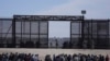 FILE - Migran yang melintasi perbatasan dari Meksiko ke AS menunggu di samping tembok perbatasan AS tempat agen Patroli Perbatasan AS berjaga, terlihat dari Ciudad Juarez, Meksiko, Kamis, 30 Maret 2023. ( AP/Fernando Llano, File)