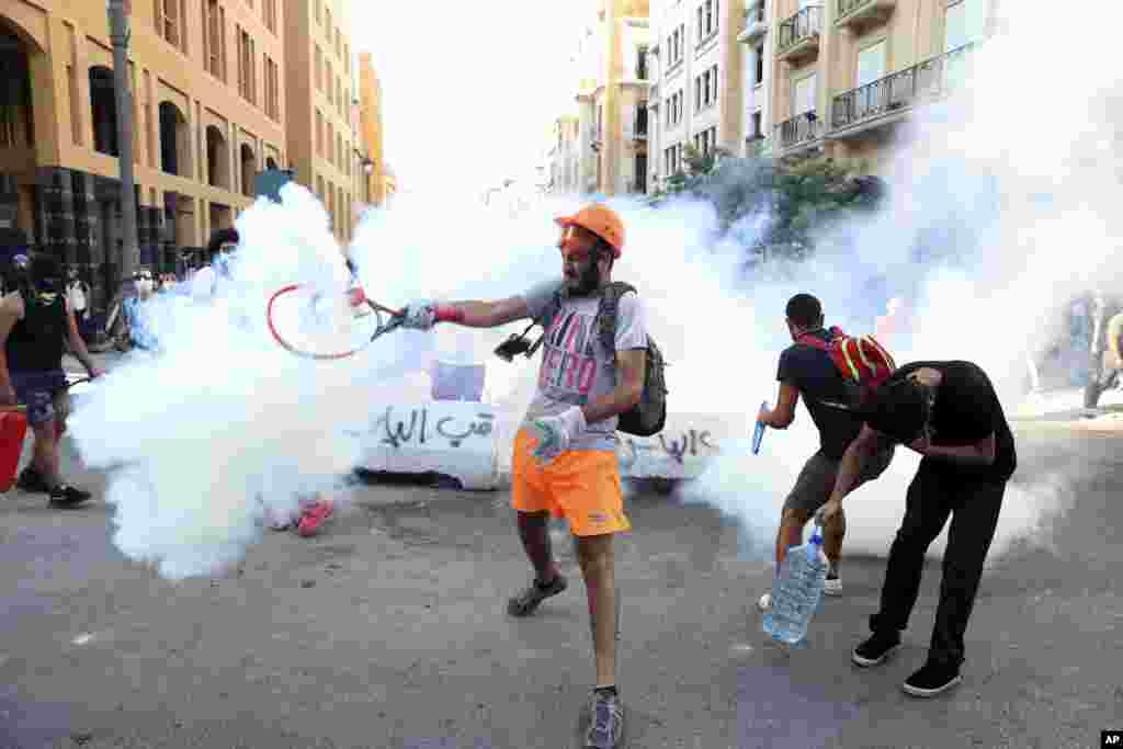 An anti-government protester uses a a tennis racket to hit back a tear gas canister at riot police during a protest following last Tuesday's massive explosion which devastated Beirut, Lebanon.