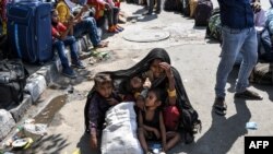Una mujer cubre a sus hijos con un chal para protegerlos del sol mientras espera con otros trabajadores migrantes y familias para registrarse en un tren que va a sus lugares de origen.