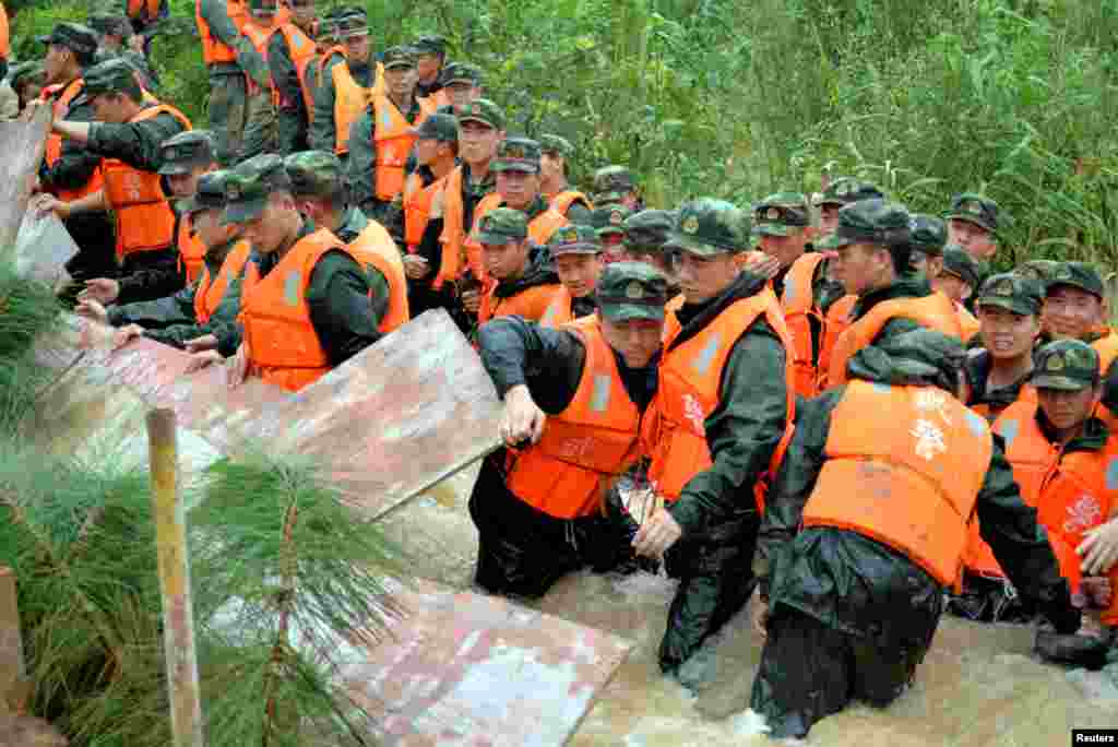 Para anggota polisi paramiliter berusaha membendung air banjir di kota Nanjing, Jiangsu, China.