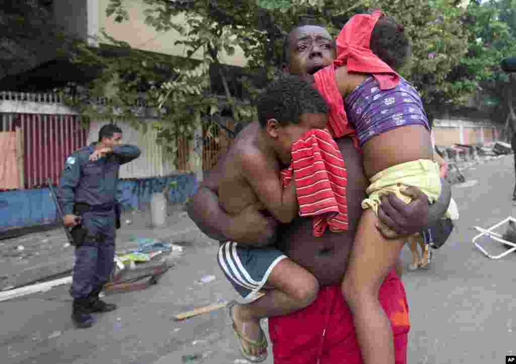 Seorang laki-laki berlari sambil menggendong dua anak ketika terjadi penggusuran di Rio de Janeiro, Brasil. Para penghuni liar di Rio de Janeiro bentrok dengan polisi setelah pengadilan Brasil memerintahkan 5.000 orang diusir dari bangunan-bangunan yang ditinggalkan oleh perusahaan telekomunikasi. 