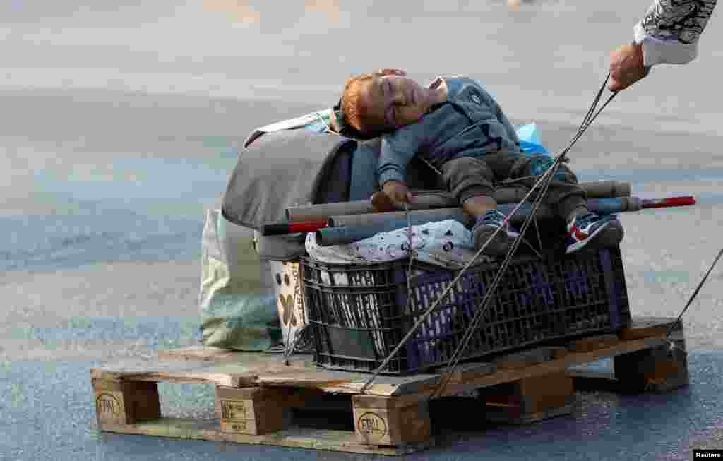 A woman pulls a baby on a pallet as they move to a new temporary camp for migrants and refugees, on the island of Lesbos, Greece, Sept. 21, 2020.
