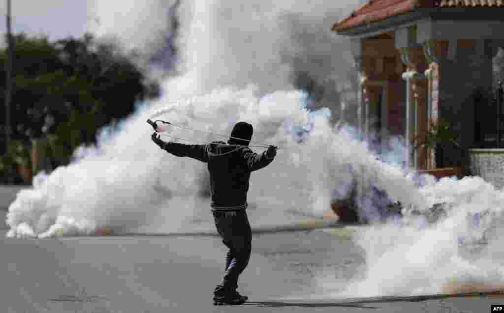 Seorang laki-laki Palestina menggunakan katapelnya untuk melemparkan kembali tabung gas air mata ke arah para tentara Israel dalam bentrokan di desa Silwad, Tepi Barat, di utara Ramallah. 