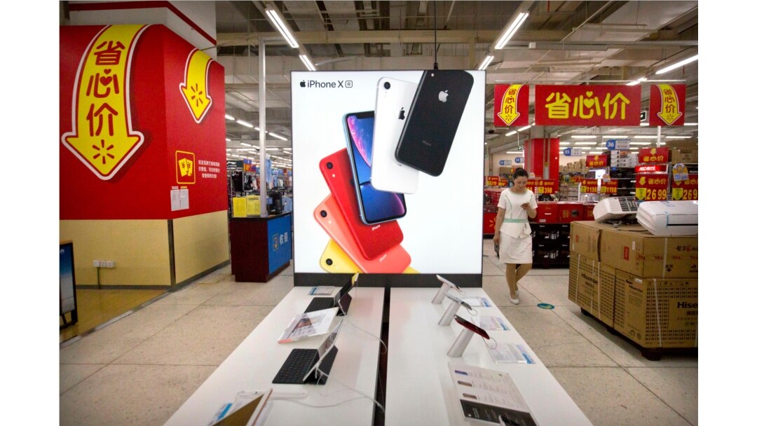 A woman uses her smartphone as she walks past a display for the Apple iPhone XR at a supermarket in Beijing, Tuesday, May 14, 2019. Sending Wall Street into a slide, China announced higher tariffs Monday on $60 billion worth of American goods.