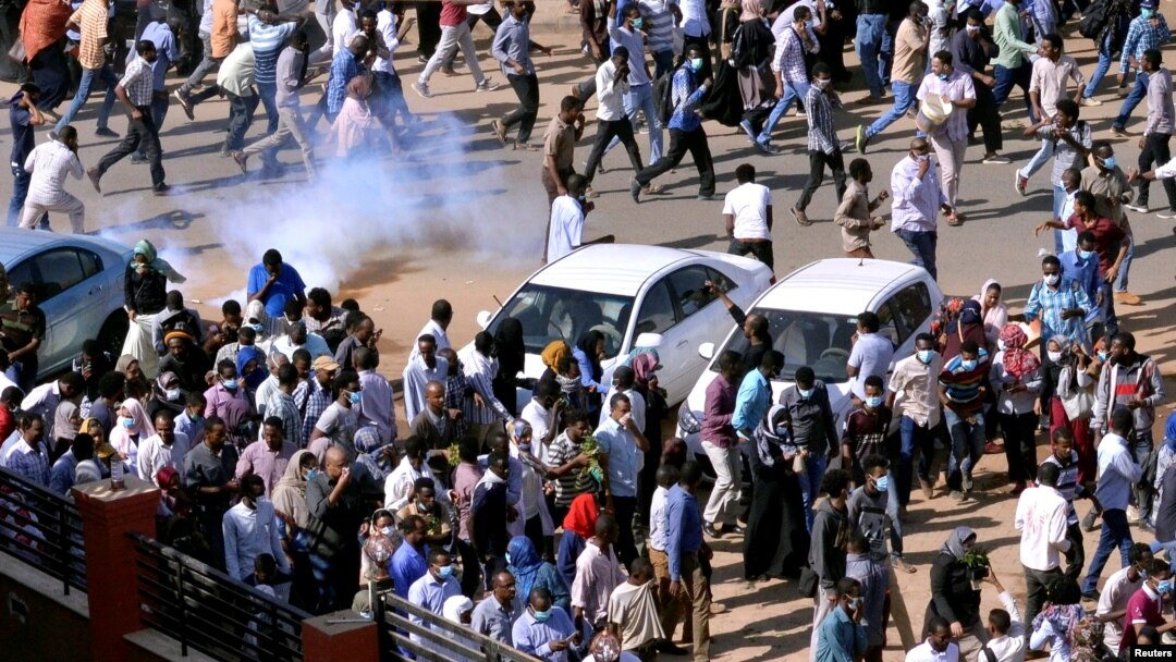FILE - Demonstrators run from teargas lobbed to disperse them as they march along the street during anti-government protests in Khartoum, Sudan, Dec. 25, 2018. 