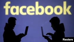 FILE - Silhouettes of laptop users are seen next to a screen projection of Facebook logo in this picture illustration taken March 28, 2018.